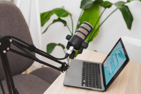 В современном офисном помещении микрофон устанавливается на руку, расположенную рядом с ноутбуком с изображением подкаста. Эта установка идеально подходит для участия в образовательных дискуссиях.