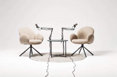 Küçük bir masanın etrafına podcast röportajı için iki rahat sandalye yerleştiriliyor. Mikrofonlar ayarlanabilir kollara yerleştirilmiş. Tartışmalar için davetkar bir ortam yaratıyorlar..