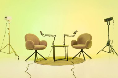 Podcast kurulumu birbirine bakan iki rahat sandalyeyi gösteriyor, konuşmaya hazır mikrofonlarla donatılmış..