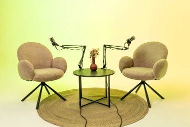 Küçük bir masanın etrafında podcast tartışmasına hazır iki rahat sandalye var. Her sandalye ayarlanabilir bir kolda yumuşak bir gradyan arka plana ayarlı bir mikrofon ile donatılmıştır..