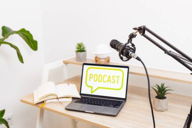 İyi hazırlanmış bir çalışma alanı, ayarlanabilir bir standda bir mikrofonun yanında podcast logosu gösteren bir dizüstü bilgisayarı vurgular.