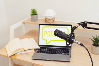 İyi düzenlenmiş bir çalışma alanı, bir standa bağlı bir mikrofon, PODCAST sözcüğünü gösteren bir dizüstü bilgisayar ve röportaj veya eğitim dersleri vermek için mükemmel bir not defteri içerir..