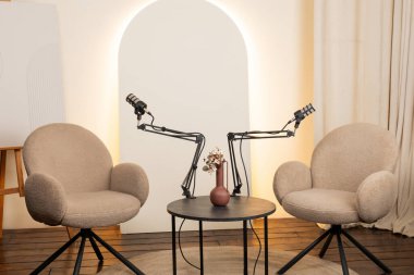 Konforlu podcast stüdyosu birbirine bakan iki rahat sandalyeyi içeriyor. Röportajlar için ayarlanabilir mikrofonlar ve sıcak bir ortamda anlamlı konuşmalar..