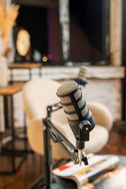 Şık bir yayın stüdyosunda, podcast oturumları için rahat bir sandalyenin yanına birden fazla mikrofon yerleştirilir. Ortam sıcak ve davetkar. Tartışmak için ideal..