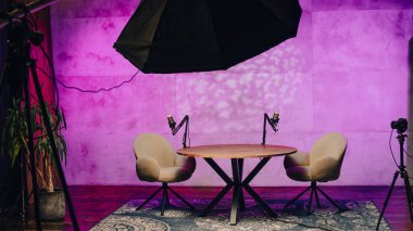 İyi tasarlanmış bir podcast stüdyosunda, iki rahat sandalye yuvarlak bir masaya yerleştirilir. Mikrofonlar ve büyüleyici ışıklandırmayla donatılmış bu alan dinamik konuşmaları ve dersleri davet eder..