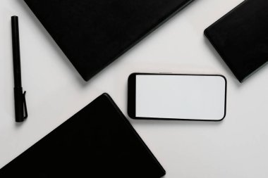 Bir çalışma alanı, üretkenlik için organizasyon ve planlamanın önemini vurgulayan, beyaz bir yüzeyde düzgün bir şekilde düzenlenmiş akıllı telefon, planlayıcı ve defter sergiler..
