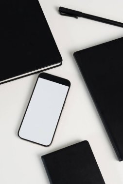 Bir cep telefonu, çeşitli siyah defterler ve kalemle birlikte temiz bir yüzey üzerinde uzanır. Bu, planlama ve not alma için verimli bir çalışma alanı sunar..