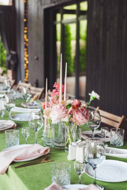 Güzel düzenlenmiş bir düğün masasında zarif cam eşyalar, çiçekli süsler ve yumuşak ışıklandırma konuklar için romantik ve davetkar bir ortam yaratıyor..