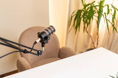 Podcast için iyi ışıklandırılmış bir odada ayarlanabilir bir kolda yüksek kaliteli bir mikrofon boş bir sandalyenin yanında, davetkar bir tartışma ve yaratıcılık..