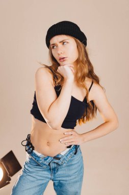 Kendine güvenen bir model, stüdyoda poz verirken modaya uygun bir kıyafet sergiler. Tarafsız bir zemine karşı durduğu için yüz ifadesi ve modasına odaklanmış durumda..