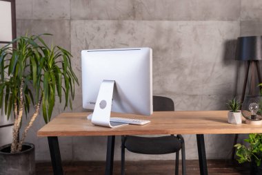 Temiz ve modern bir ofis çalışma alanı ahşap bir masanın üzerinde parlak bir bilgisayar sergiliyor. Kapalı alandaki bitkiler profesyonel atmosfere biraz yeşillik katıyor..