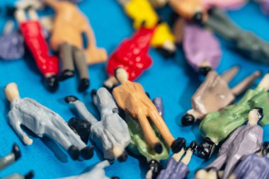 Renkli minyatür heykelcikler mavi bir yüzeye saçılmış, kaotik ama organize olmuş bir kalabalığı temsil ediyorlar. Bu soyut sahne çeşitlilik ve sosyal parçalanma temalarını vurgular.