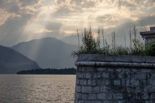 Gölün üzerinden akan güneş ışığı ve arka planda dağlar olan taş duvar.