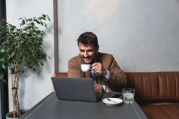 Young business man freelancer financial expert using his lunch and coffee break to talk about work with his happy satisfied client on video call on laptop. Businessperson conversation with office team