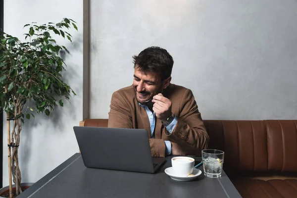 Young business man freelancer financial expert using his lunch and coffee break to talk about work with his happy satisfied client on video call on laptop. Businessperson conversation with office team