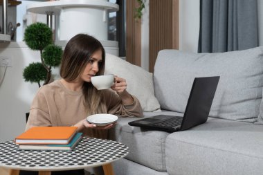 Genç değişim öğrencisi evinde çay ya da kahve içerken bilgisayardan ailesiyle başka bir ülkede konuşuyor. Bilgisayar programcısı evde işe ara veriyor.. 