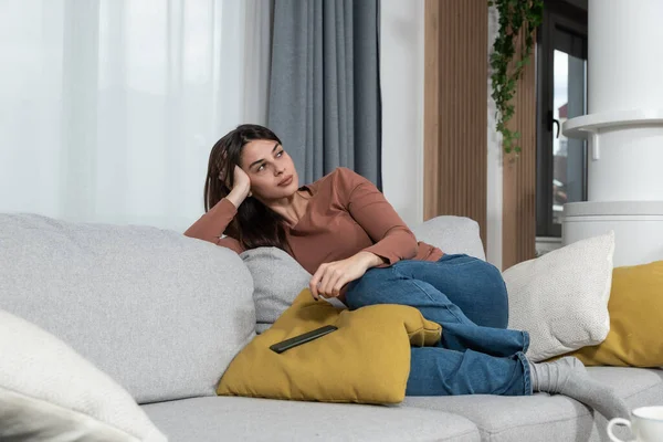 Young frustrated woman with serious facial expression sitting on the sofa at home with dropped smartphone after she had argue over the phone with her boyfriend.