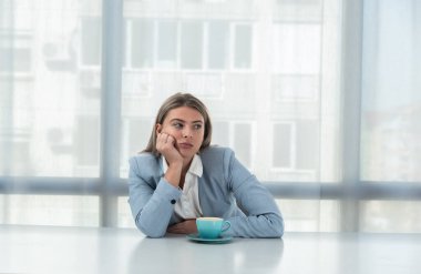 Ama önce kahve. Resmi görevdeki genç yorgun iş kadını ofiste boş bir masada kahve içerken giyiniyor. Beyaz yakalı kadın işçi, serbest çalışan mali uzman sabah rutini..