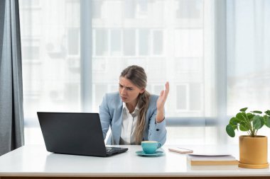Sinirli ve kızgın serbest çalışan iş kadını görüntülü konuşma, kadının tartışması ve dizüstü bilgisayara bakması, online iş konferansı. Ofis masasında oturan, şık giysili bir kadın.