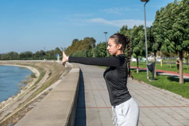 Genç kendini beğenmiş genç kız fitness egzersizleri sağlıklı yaşamın farkındalığı için sabah rutini olarak açık havada yapılır. Antrenmandan önce kaslarını esneten iyi bir kadın..