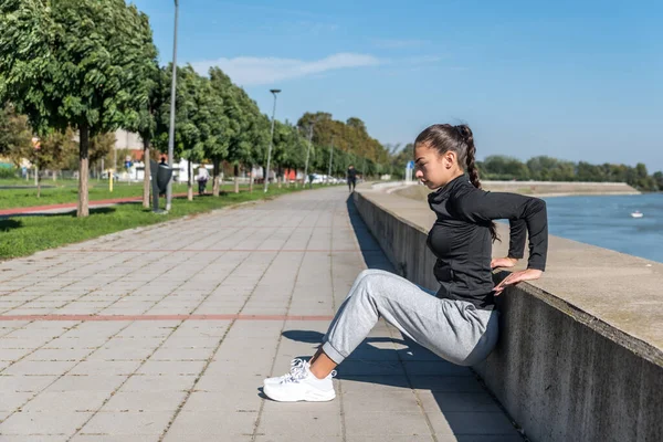 Young self loved teenage girl fitness exercises outdoor as morning routine for self-awareness of healthy life. Good posture woman stretching her muscles before workout training.