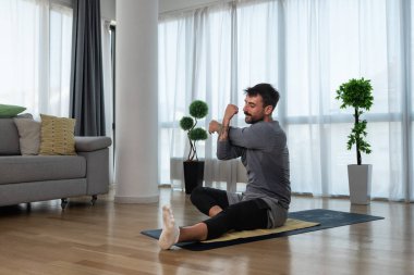 Kanserden kurtulan genç adam evde yoga antrenmanı yapıyor, kaslarını esnetiyor ve uzun süre acı ve hastalıkla mücadele ettikten sonra sağlıklı bir yaşam için egzersiz yapıyor. Meditasyon için ısınma egzersizleri.