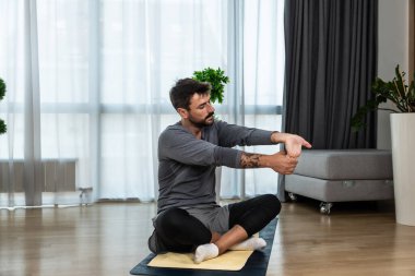 Kanserden kurtulan genç adam evde yoga antrenmanı yapıyor, kaslarını esnetiyor ve uzun süre acı ve hastalıkla mücadele ettikten sonra sağlıklı bir yaşam için egzersiz yapıyor. Meditasyon için ısınma egzersizleri.