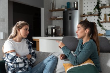 Two young women friends roommates business partners and owners of a small business are arguing at home due to the inappropriate spending of money and increased expenses on household bills.