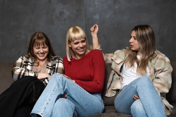 Three young female friends, roommates from college are sitting on the sofa and laughing because they are happy and successful in their lives.