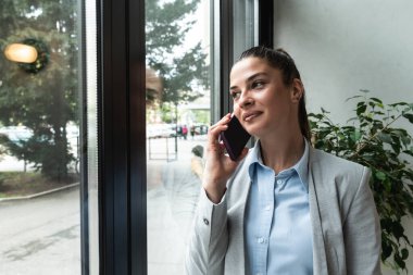 Business woman chatting online on smart-phone at window glass, typing text message, touching touchscreen keyboard, using messenger application. Millennial user holding mobile phone, close up