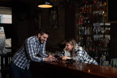 Young colleagues bartenders and waitress sit at the bar and get bored while the cafeteria is empty, spend time talking until the first guests arrive