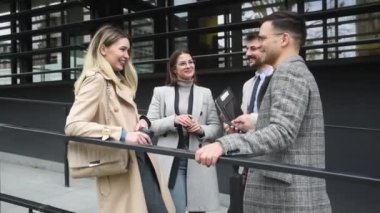 Ofis binasının önünde duran genç iş adamları, başarı hakkında deneyim paylaşımı, iş fikirleri ve çalışanların ve müşterilerin çalışma koşullarını iyileştiren öneriler hakkında konuşuyor.