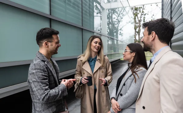 Quick briefing before meeting. Group of cheerful young successful business people talking to each other while walking outdoors. Office workers experts exchanging ideas