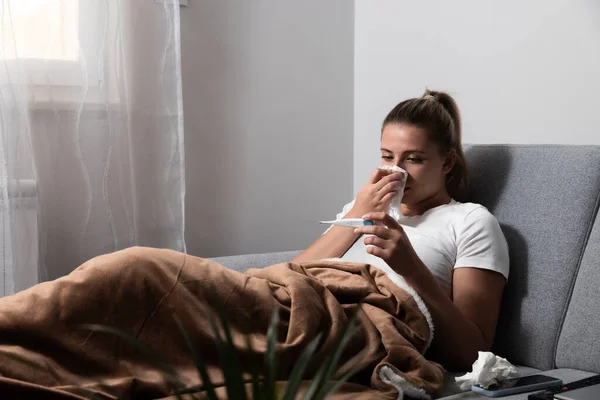 女人感冒了 在组织里打喷嚏头疼 病毒药物 年轻女子被冷吹鼻涕感染在手巾上 坐在沙发上头疼的病女 — 图库照片