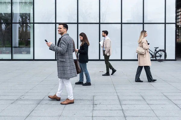 Think different concept. Group of business people in front of office building one business person walking in opposite direction from other employees. Be independent different stand out from the crowd