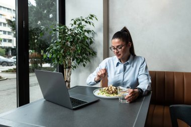 Cafe restoranında dizüstü bilgisayar kullanan takım elbiseli genç ve meşgul bir iş kadını. Aç yönetici çevrimiçi çalışıyor çevrimiçi pazarlama işlemleri ya da elkazanımları üzerinde düşünüyor