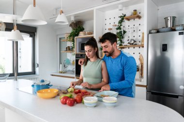 Mutlu genç çift sağlıklı organik yiyecekler hazırlarken mutfakta eğleniyor. Güzel sporcular evdeki mutfakta vejetaryen yemeği pişirirken konuşuyor ve gülümsüyor..
