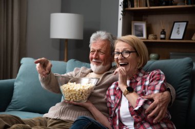 Gülen yaşlı çift, erkek ve kadın tv, komedi gösterisi veya film izlerken ve patlamış mısır çerez yeme, evde rahat kanepede oturan, olgun aile, erkek ve kadın boş zaman zevk, hafta sonu birlikte