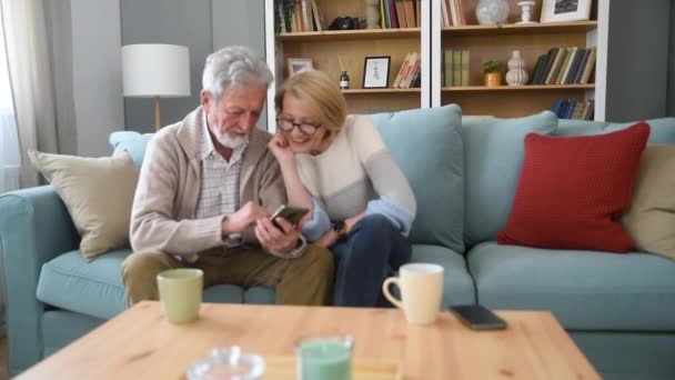 两个年长的男人和女人坐在沙发上 看着一张全家福照片 微笑着拥抱着 孩子们的回忆和怀旧情绪在国外与家人一起过着更好的生活 — 图库视频影像