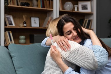 Hamilelik testi tutan çok mutlu genç bir kadın annesine hamile olduğunu ve bir bebek sahibi olacağını söylüyor. Müstakbel büyükanne ve anne kanepede mutlu.