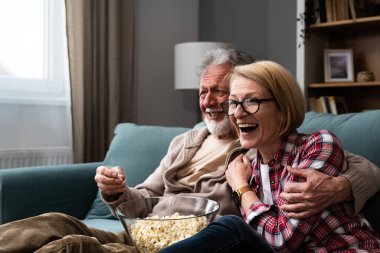 Gülen yaşlı çift, erkek ve kadın tv, komedi gösterisi veya film izlerken ve patlamış mısır çerez yeme, evde rahat kanepede oturan, olgun aile, erkek ve kadın boş zaman zevk, hafta sonu birlikte