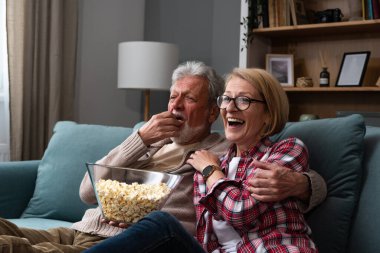 Gülen yaşlı çift, erkek ve kadın tv, komedi gösterisi veya film izlerken ve patlamış mısır çerez yeme, evde rahat kanepede oturan, olgun aile, erkek ve kadın boş zaman zevk, hafta sonu birlikte