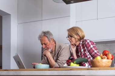 Üst düzey çiftler evde organik sebzeler pişirirken dizüstü bilgisayarda internetten yemek tarifi okuyup hazırlıyorlar.