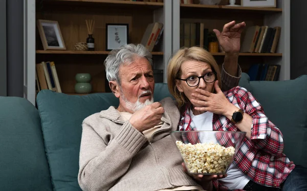 stock image Elderly couple watching bad news, quiz or competition with displeasure and expression while eating popcorn. Senior people husband and wife watch political debate at home making negative faces