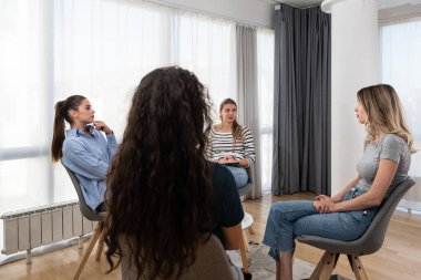 Mutlu, gülümseyen kadın koç, terapist ya da iş dünyası yöneticisi grup terapisi seansında genç kadınları destekleyip motive ediyor ya da iş yerinde kurumsal personel eğitimi toplantısı