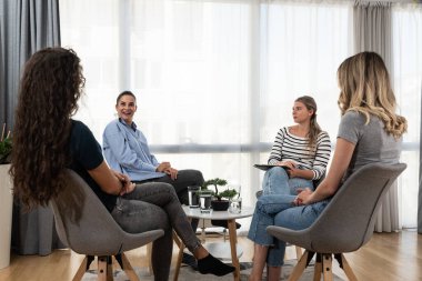 Mutlu, gülümseyen kadın koç, terapist ya da iş dünyası yöneticisi grup terapisi seansında genç kadınları destekleyip motive ediyor ya da iş yerinde kurumsal personel eğitimi toplantısı