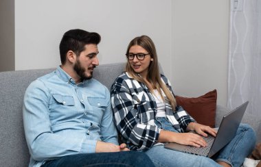 Genç mutlu çift evde birlikte bütçe planlaması, dizüstü bilgisayara notlar yazma, alışveriş listesi oluşturma ya da düğün davetiyeleri için davetli listesi hazırlama, merasim sandalyelerini sayma