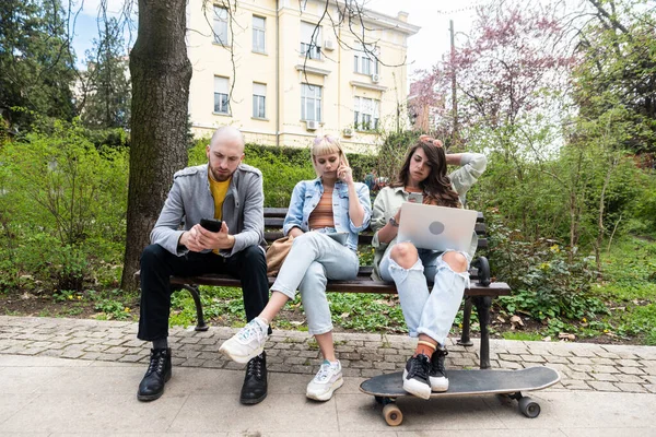 Parktaki bankta oturmuş dizüstü bilgisayarla yazı yazmaktan bahseden üç öğrenci. Eğitim konsepti. Yeni strateji işleri için fikirler ve çözümler üzerinde çalışan genç meslektaşlar