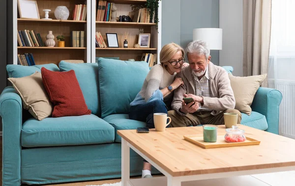 Rahat 60 'lı yaşlarda bir kadın ve 70' li yaşlarda yaşlı bir çift ellerinde akıllı telefon olan cep telefonu ile cep telefonu teknolojisi cihazında arama mesajı ekommersi sunan cep telefonu kullanan bir çift evdeki koltukta oturuyor.
