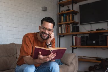 Genç adam bir antikacıda ilginç bir eski kitap bulmuş ve evinde küçük, rahat dairesinde kanepede otururken mutlu bir şekilde okuyor..